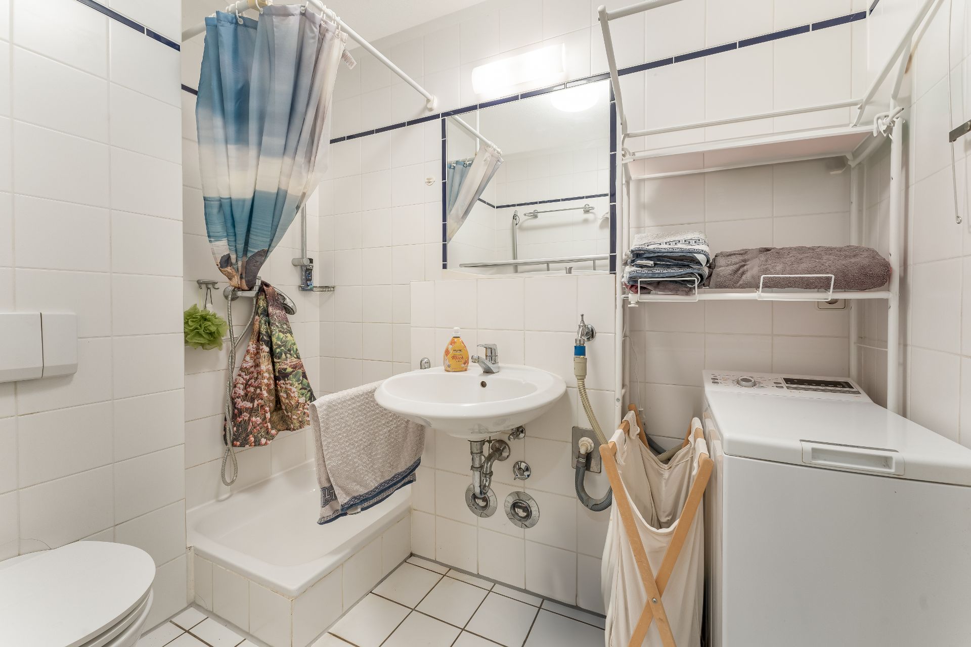 Helles Bad mit Dusche, Waschbecken, Toilette, Waschmaschine und Regal mit Handtüchern.