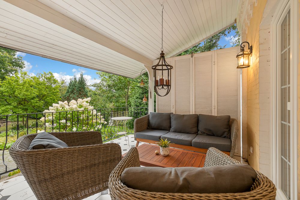 Überdachte Terrasse mit Rattanmöbeln, Holztisch und Blick auf einen grünen Garten.