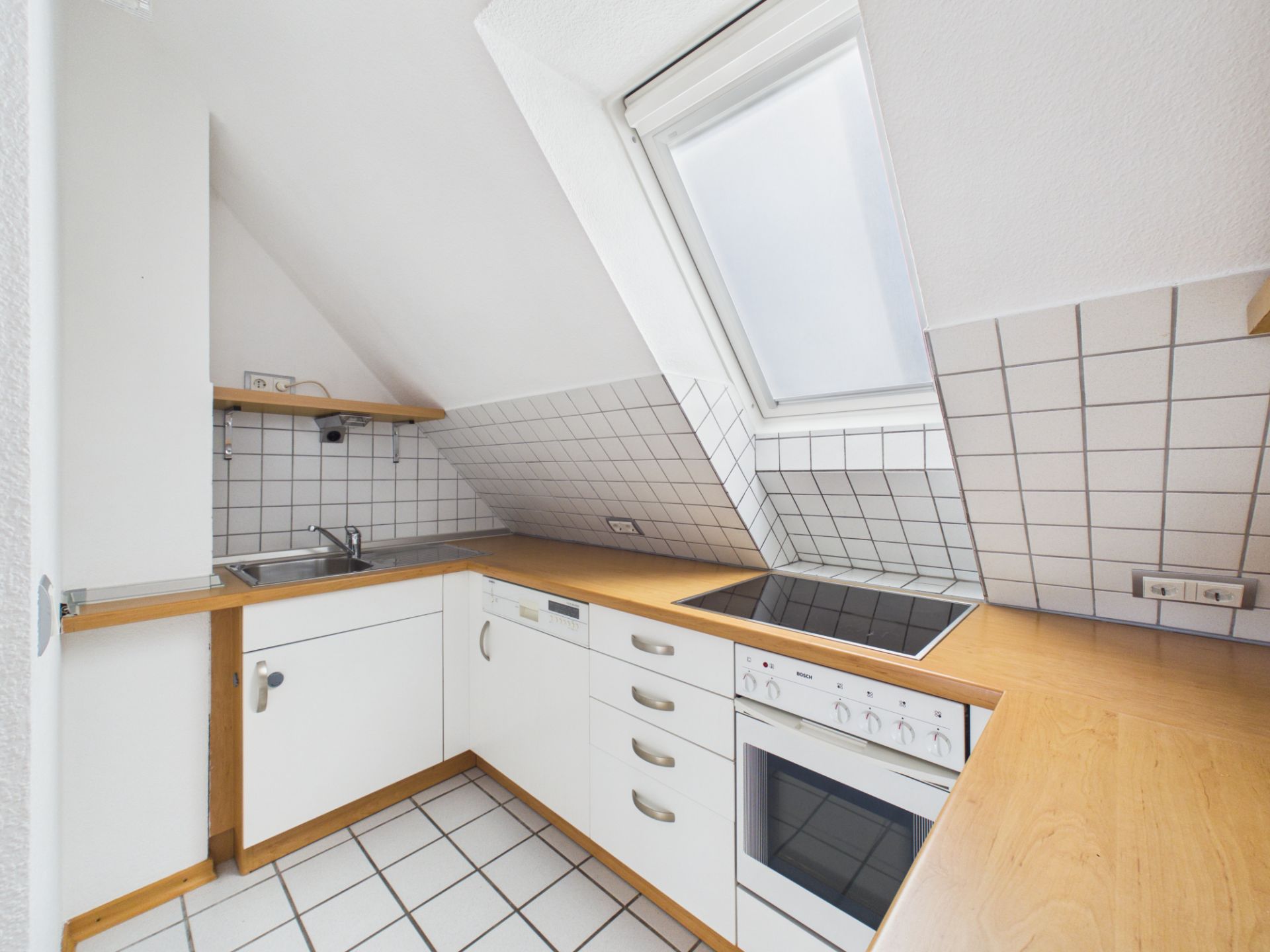 Moderne Einbauküche mit weißen Fronten, Cerankochfeld, Spüle und Dachfenster unter Schräge.