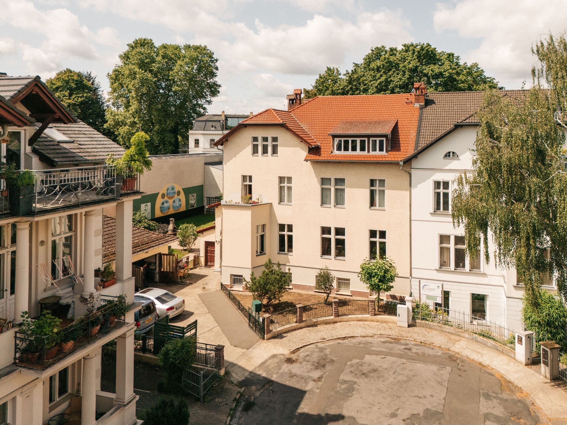 Mehrfamilienhaus mit rotem Dach und kleinem Innenhof, davor ein runder Wendeplatz.
