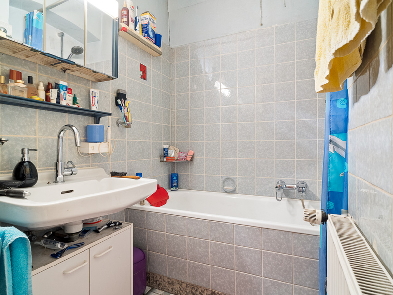 Kleines Badezimmer mit Waschbecken, Badewanne und Regal mit Pflegeprodukten.