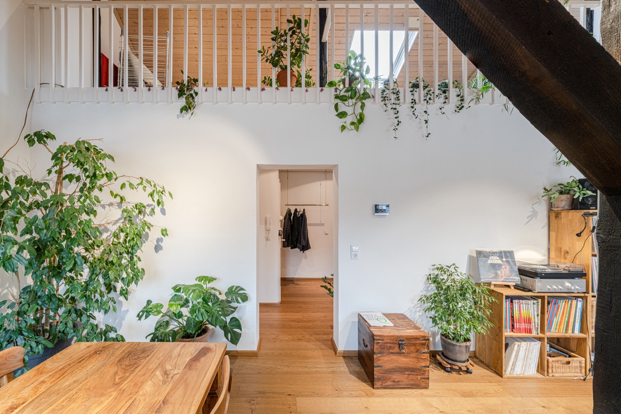 Helles Wohnzimmer mit Holzboden, Pflanzen, Holztisch, Plattenspieler und einer Treppe.