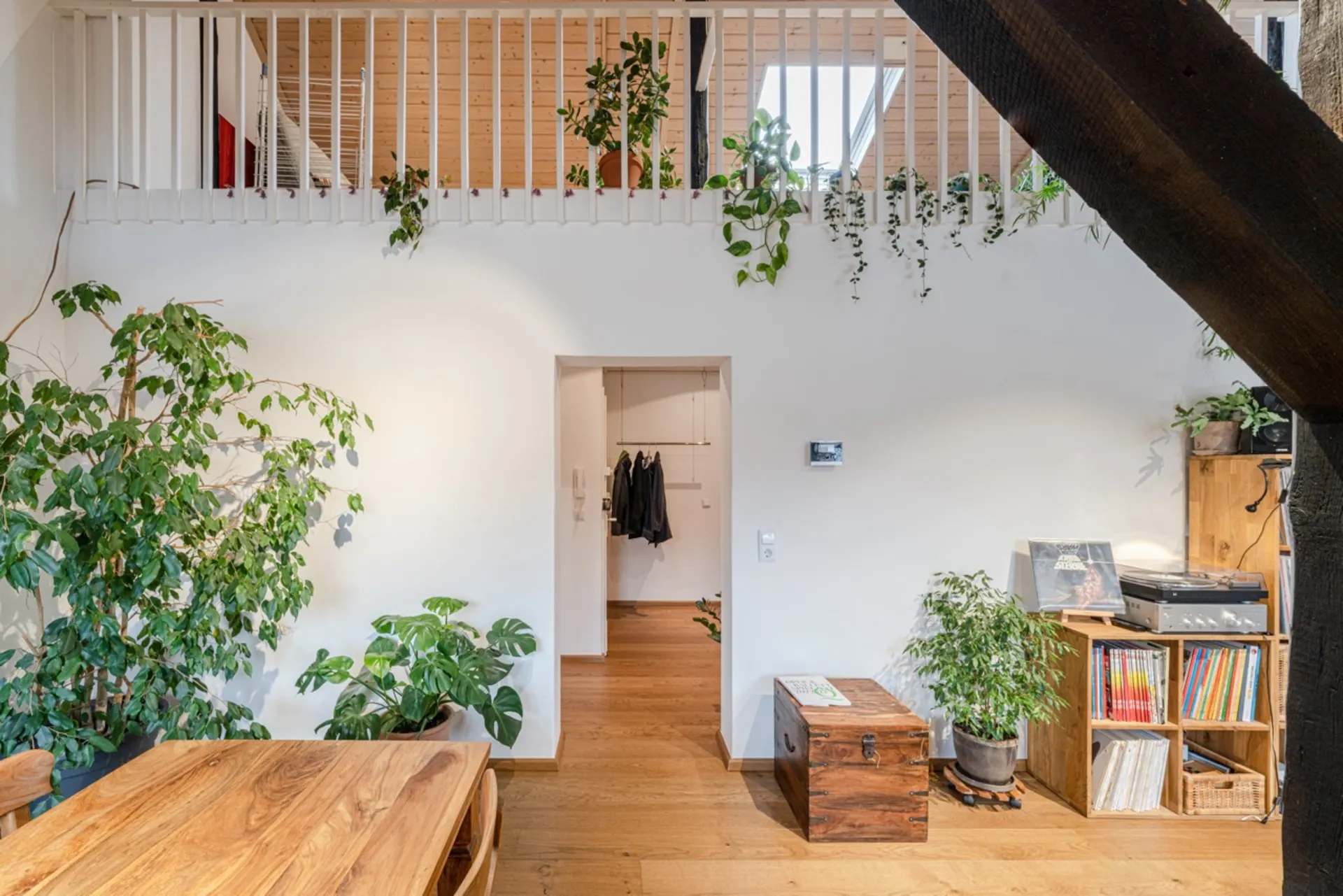 Helles Wohnzimmer mit Holzboden, Pflanzen, Holztisch, Plattenspieler und einer Treppe.