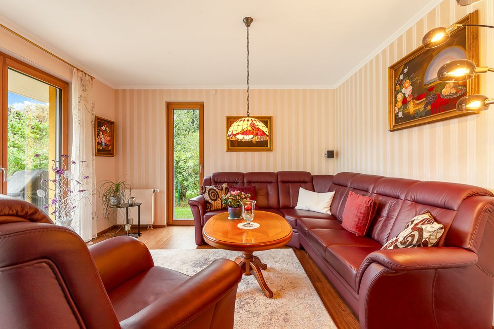 Wohnzimmer mit rotem Ledersofa, Holztisch, Lampen und Gemälden an den Wänden.