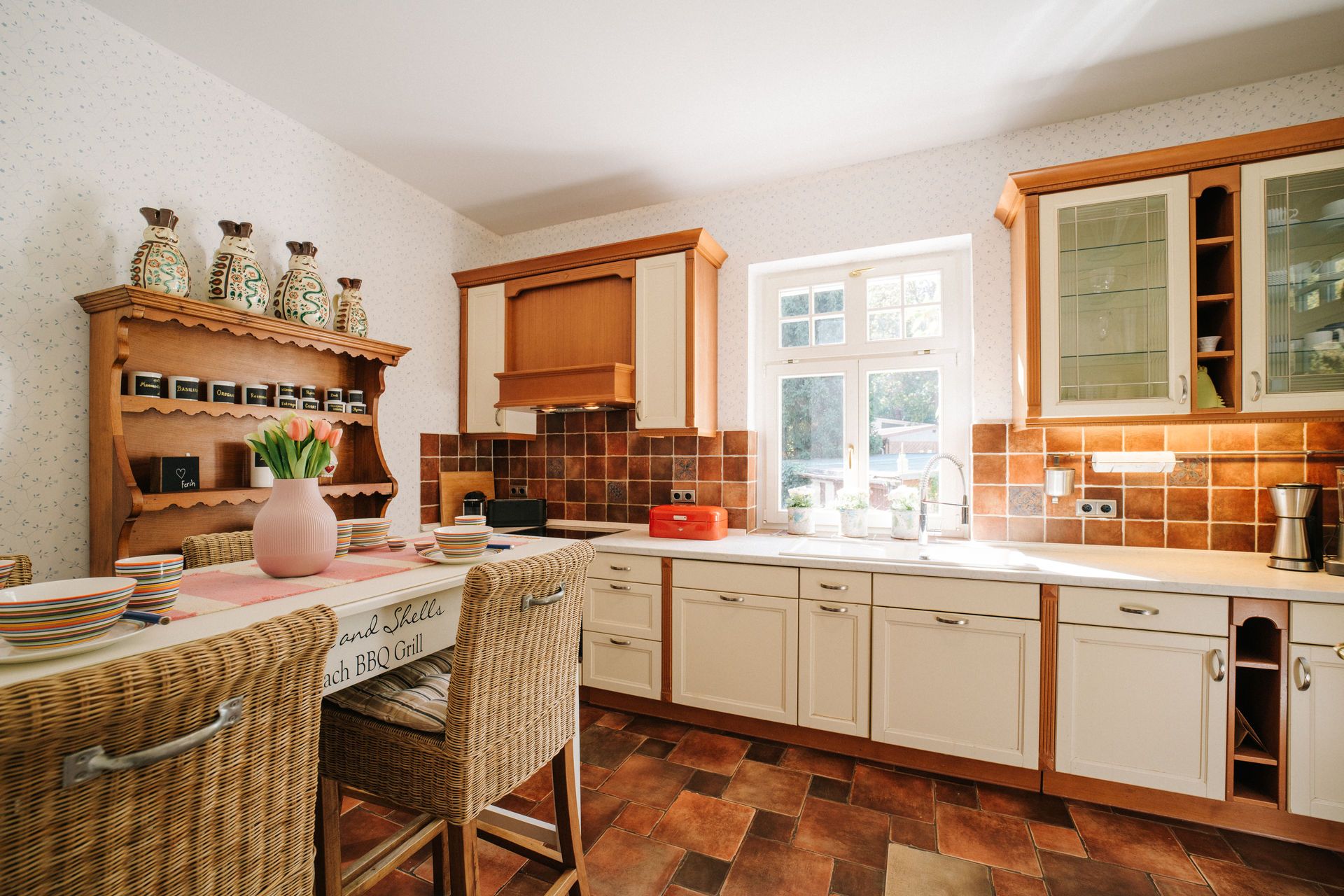 Helle Landhausküche mit Holzmöbeln, Esstheke, Fenster und gefliesten Böden.