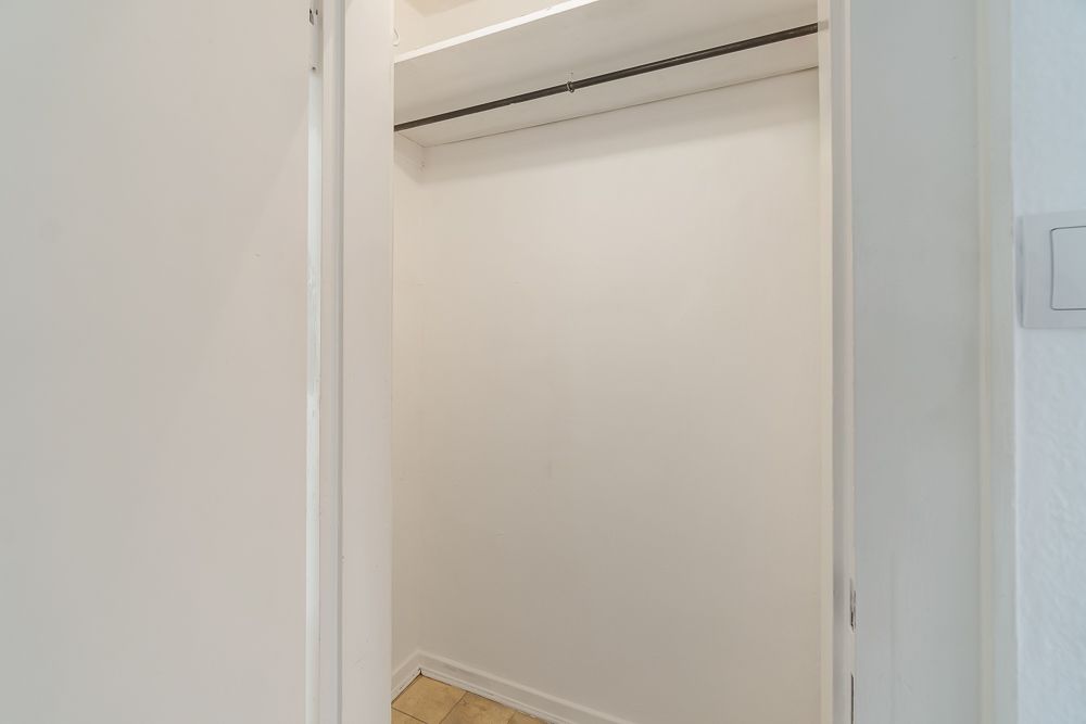 Leerer, weißer Wandschrank mit Kleiderstange und Fliesenboden.