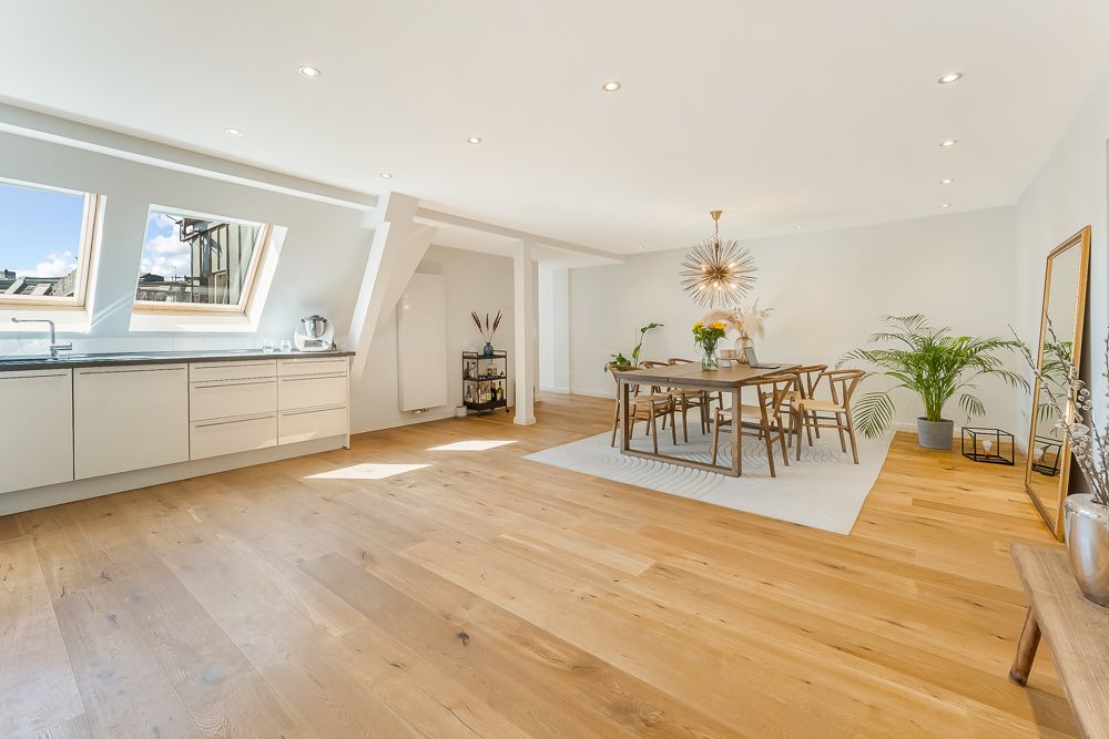 Helle, moderne Wohnküche mit Holzboden, Esstisch, Pflanzen und zwei Dachfenstern.
