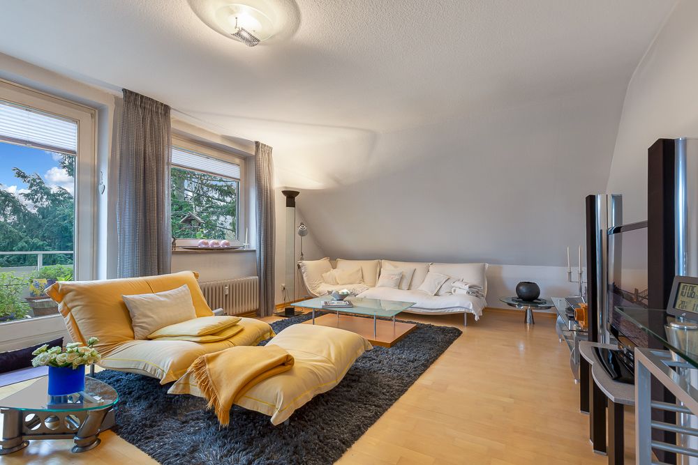 Helles Wohnzimmer mit gelbem Sessel, Ecksofa, großem Fenster und Glastisch auf Holzfußboden.