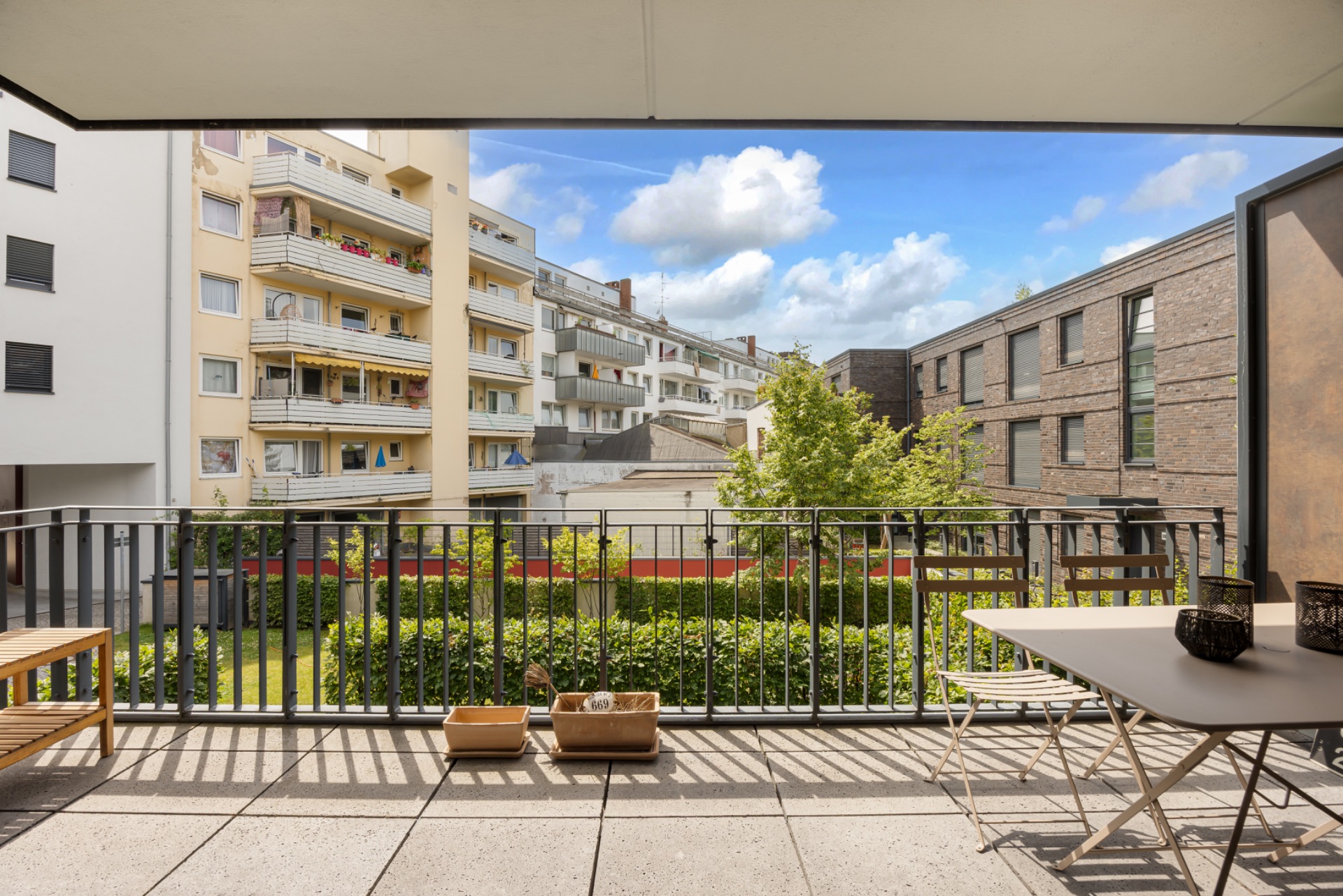 Balkon mit Sitzbank, Tisch und Blick auf Wohnhäuser und Garten bei Tageslicht.