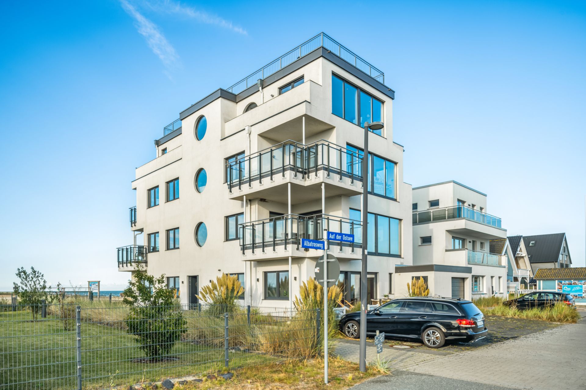 Modernes, mehrstöckiges Wohngebäude mit Balkonen und großen Fenstern, davor ein geparktes Auto.
