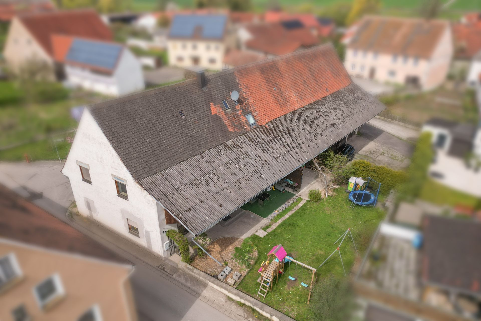 Langes Wohnhaus mit großem Garten, Schaukel, Rutsche und Trampolin im Hof, umgeben von weiteren Häusern.