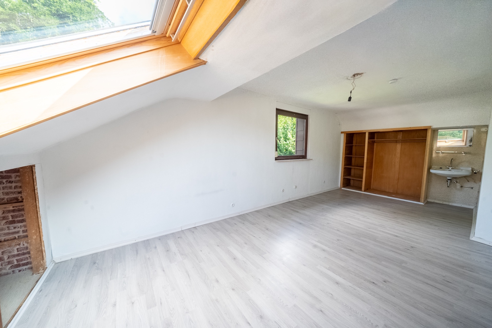 Heller Raum mit Dachfenster, Holzfußboden, offenem Regal und kleinem Waschbecken an der Wand.
