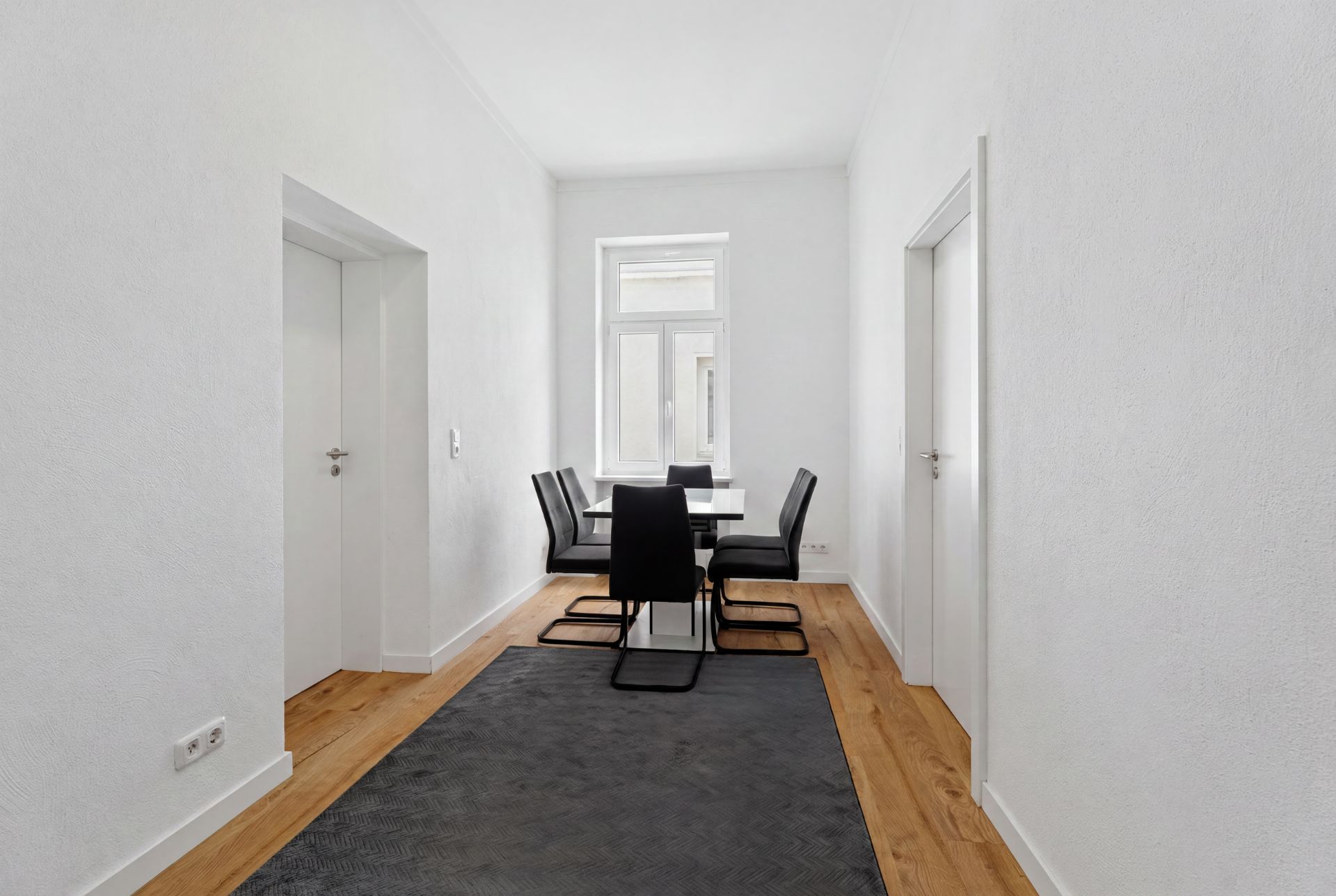 Heller Essbereich mit Tisch, sechs schwarzen Stühlen, Fenster und Holzfußboden.