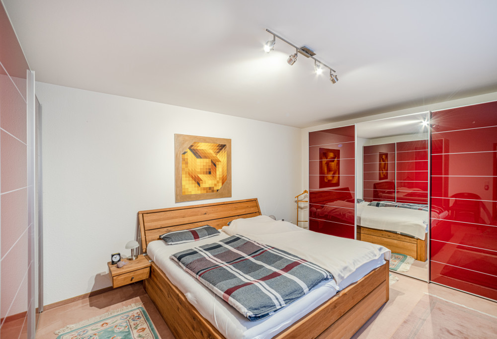 Schlafzimmer mit Holzbett, Nachttisch, modernem Kunstbild und großem Kleiderschrank mit roten Türen.