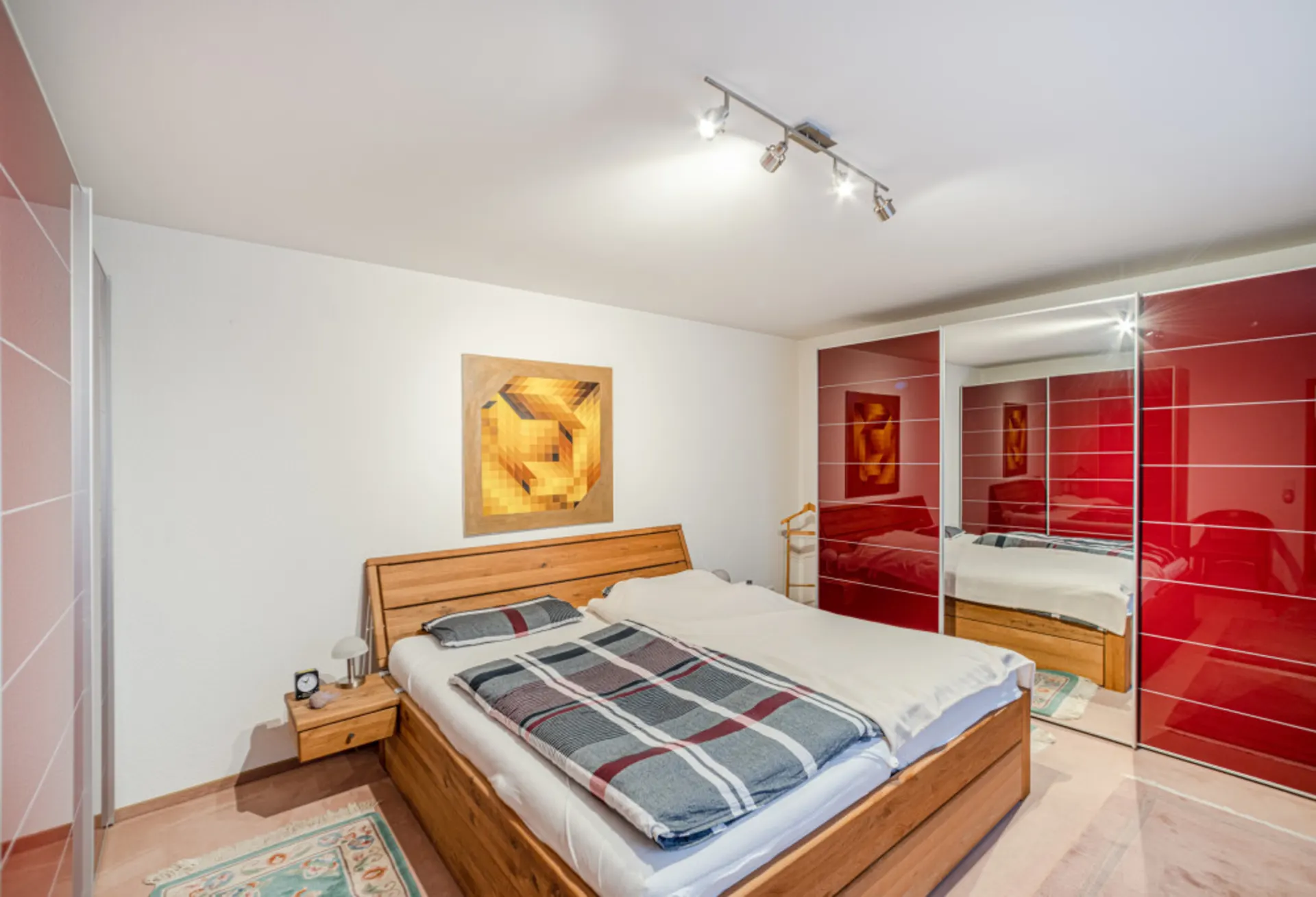Schlafzimmer mit Holzbett, Nachttisch, modernem Kunstbild und großem Kleiderschrank mit roten Türen.