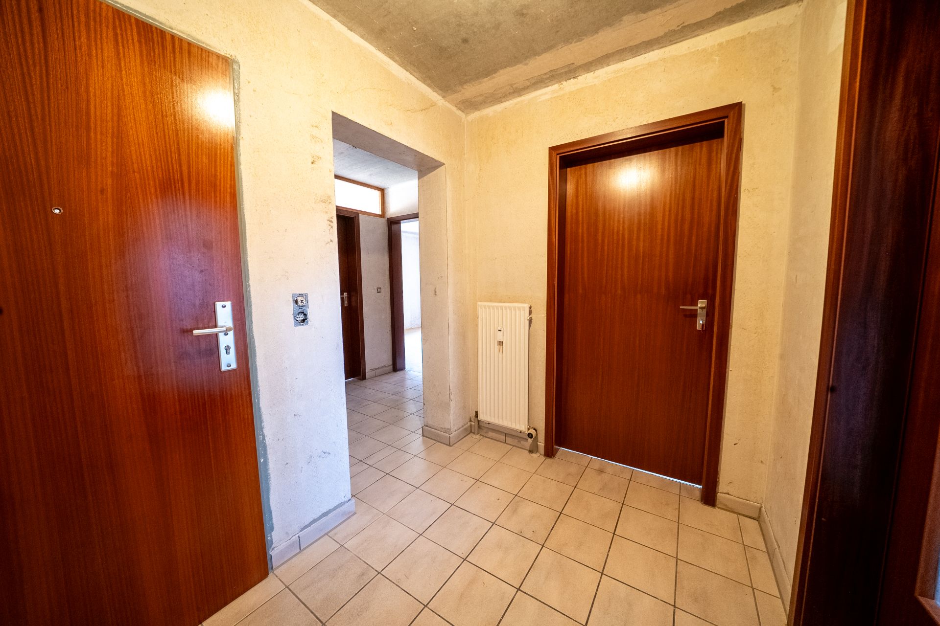 Flur mit gefliestem Boden, mehreren Holztüren und einem weißen Heizkörper an der Wand.
