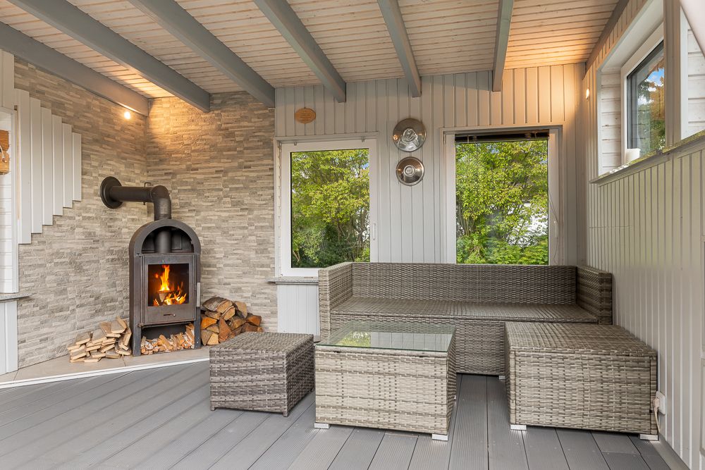 Gemütlicher Wintergarten mit Kamin, Rattan-Sofa, Glastisch und Blick ins Grüne.