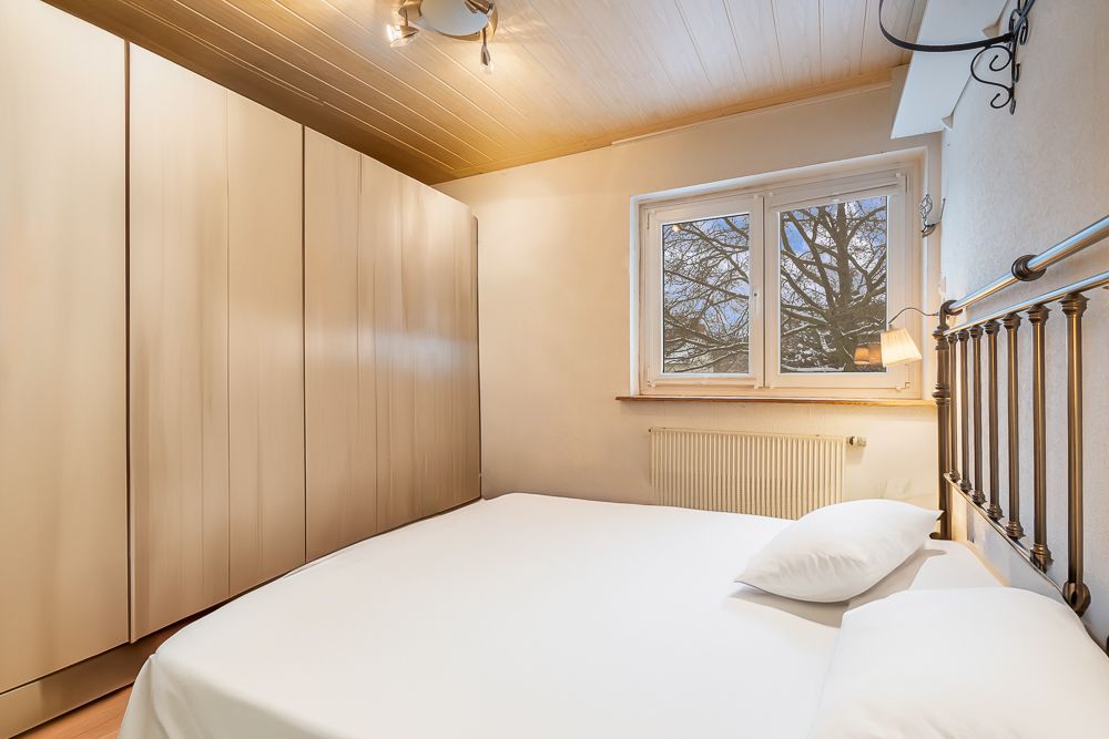Helles Schlafzimmer mit großem Bett, Kleiderschrank und Fenster mit Blick auf Bäume.