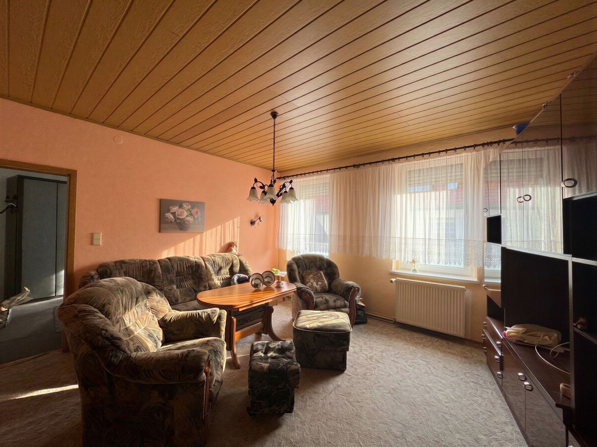 Wohnzimmer mit Polstermöbeln, Couchtisch, großem Fenster und hellem Vorhang.