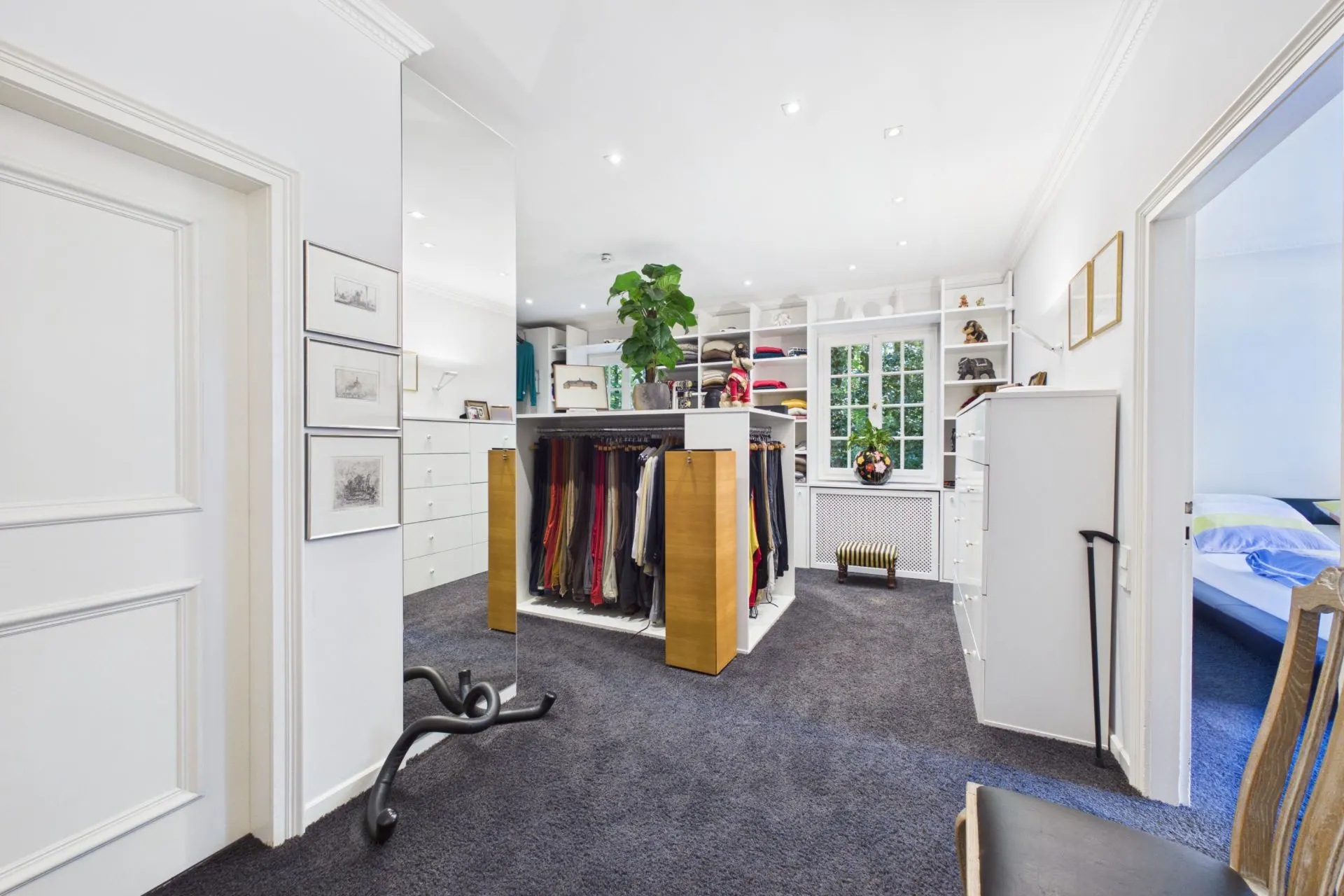 Großes Ankleidezimmer mit Kleiderschränken, Regalen und Blick auf ein Schlafzimmer.