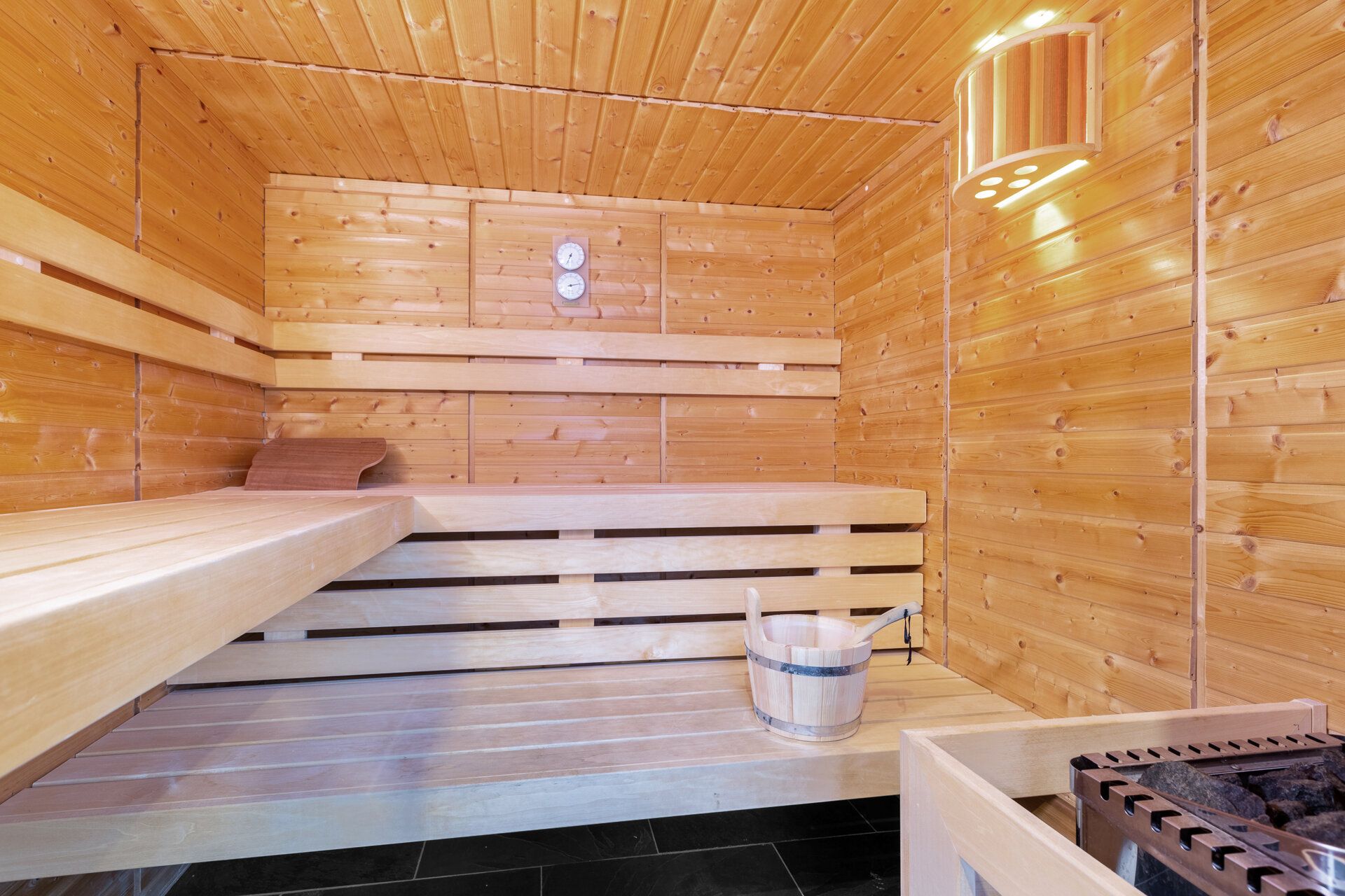 Innenansicht einer Holzsauna mit Bank, Eimer und Ofen.