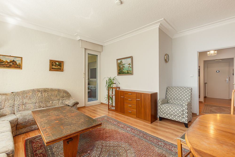 Wohnzimmer mit Teppich, Sofa, Sessel, Holztisch, Kommode und Wandbildern.