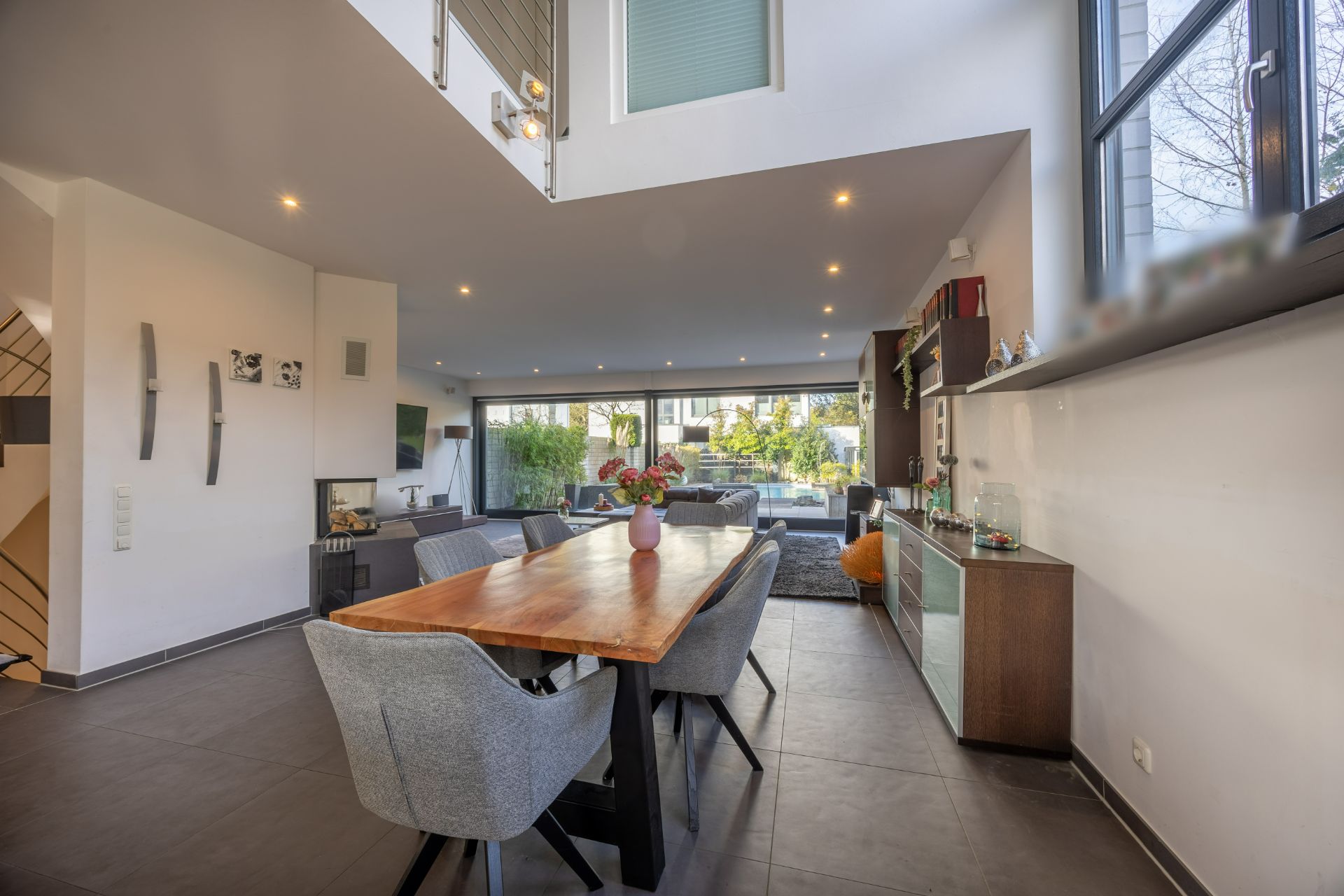 Modernes Esszimmer mit Holztisch, grauen Stühlen und großen Fenstern in einem Wohnhaus.