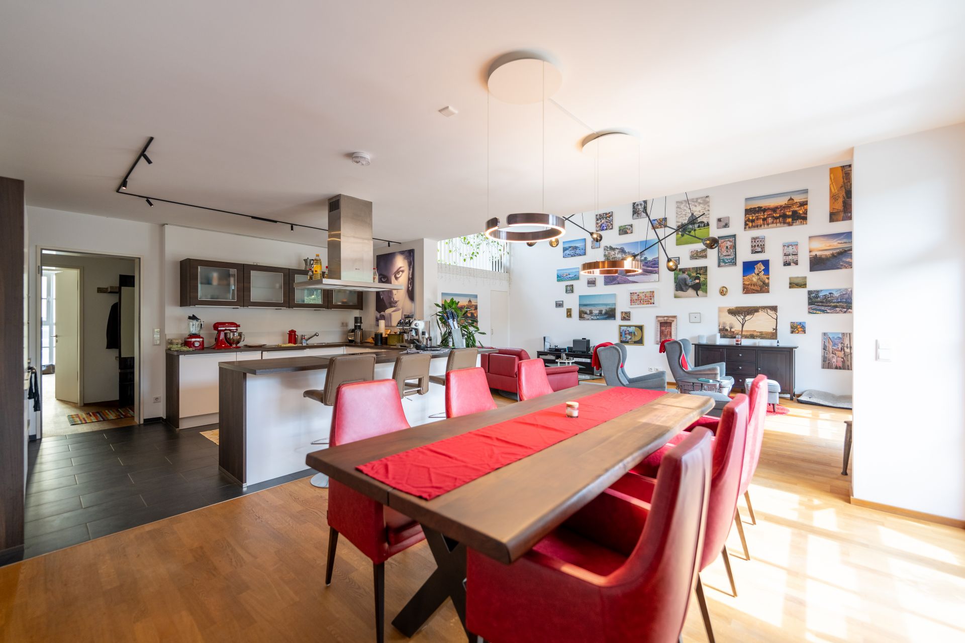 Helles Wohnzimmer mit Esstisch, roten Stühlen, offener Küche und vielen Bildern an der Wand.