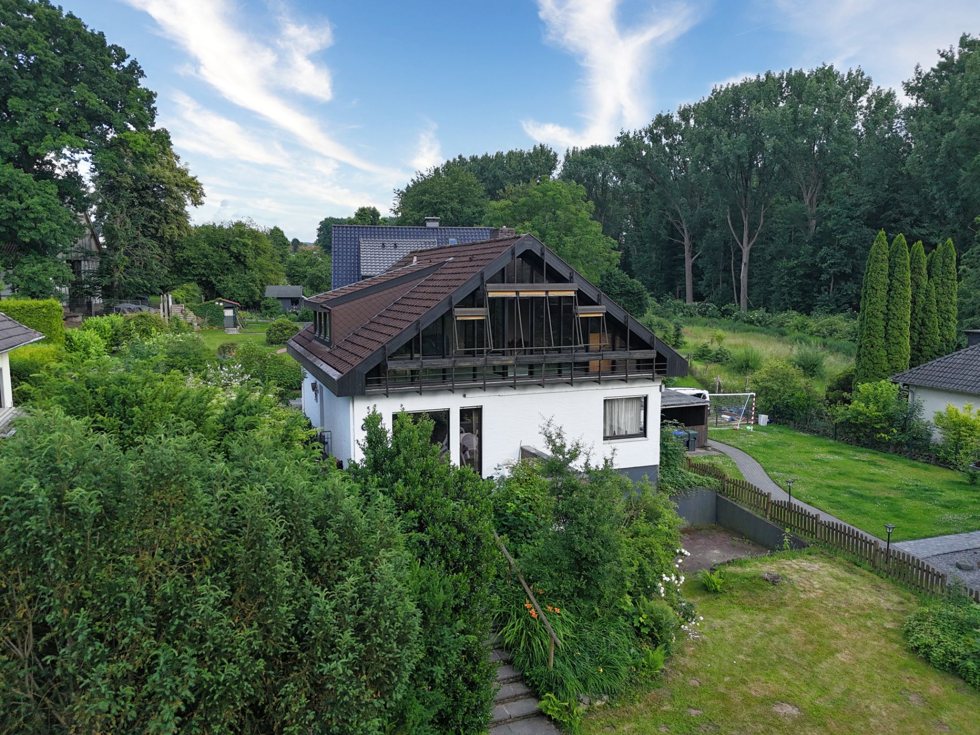 Weißes Einfamilienhaus mit Gartengrundstück und umgebenden Bäumen.
