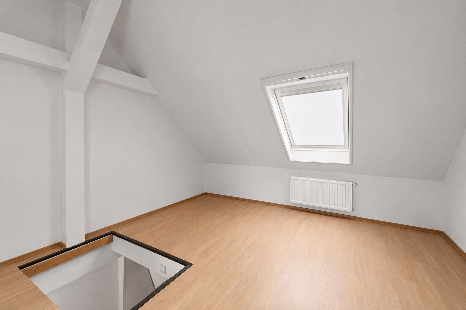 Heller Dachraum mit Holzfußboden, Dachfenster und offenem Zugang zur Treppe.