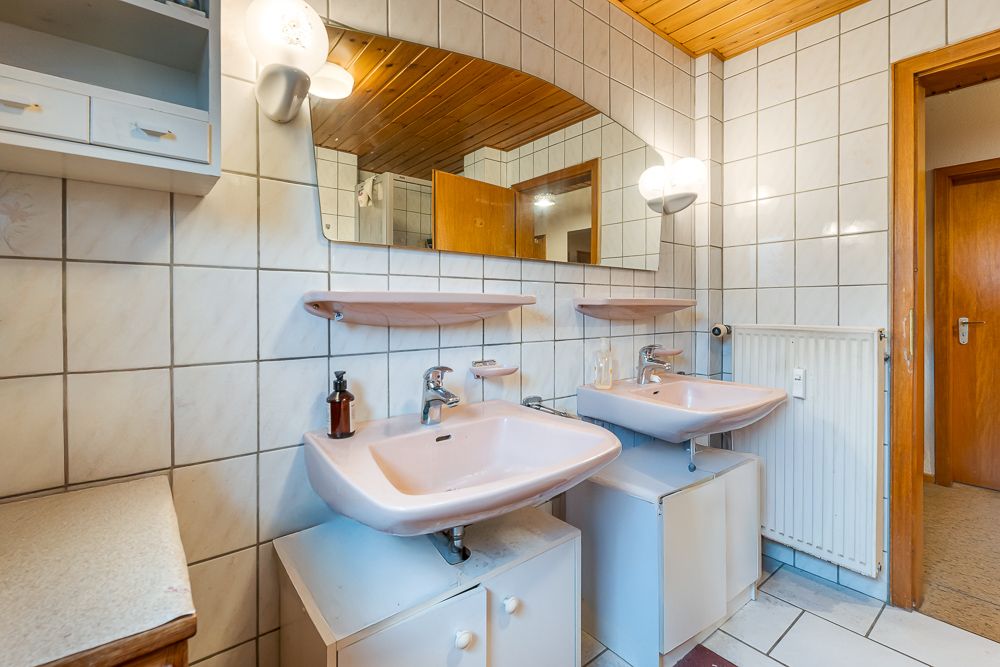 Badezimmer mit zwei Waschbecken, großem Spiegel, weißen Fliesen und Holzelementen.