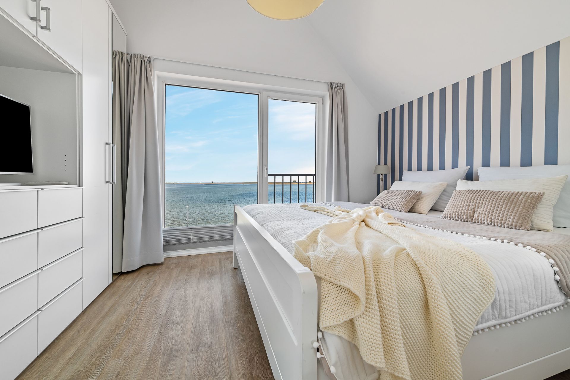 Helles Schlafzimmer mit Doppelbett, gestreifter Wand und großem Fenster mit Meerblick.