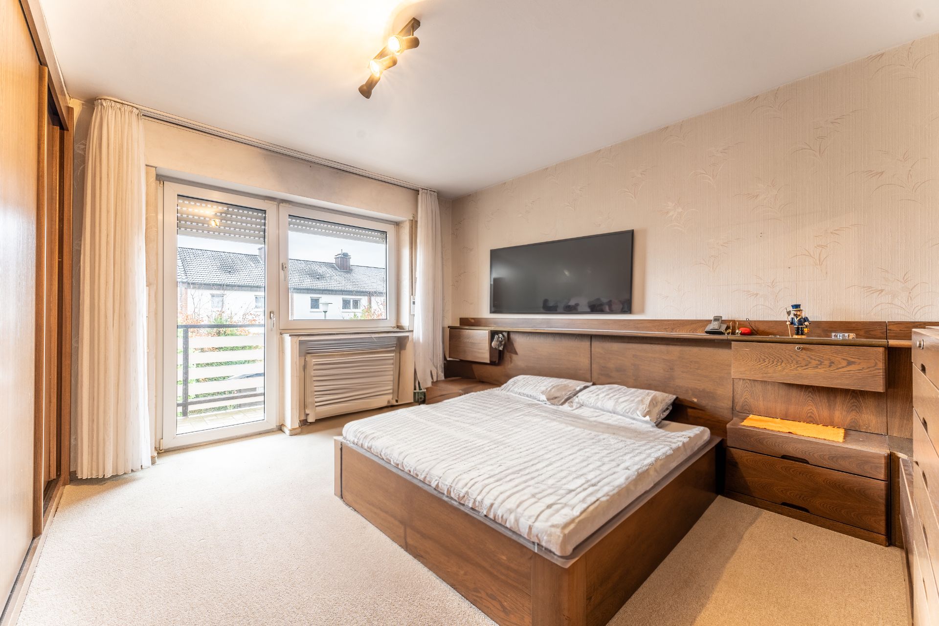 Schlafzimmer mit Doppelbett, Holzschränken, Fernseher an der Wand und Fenster mit Blick nach draußen.