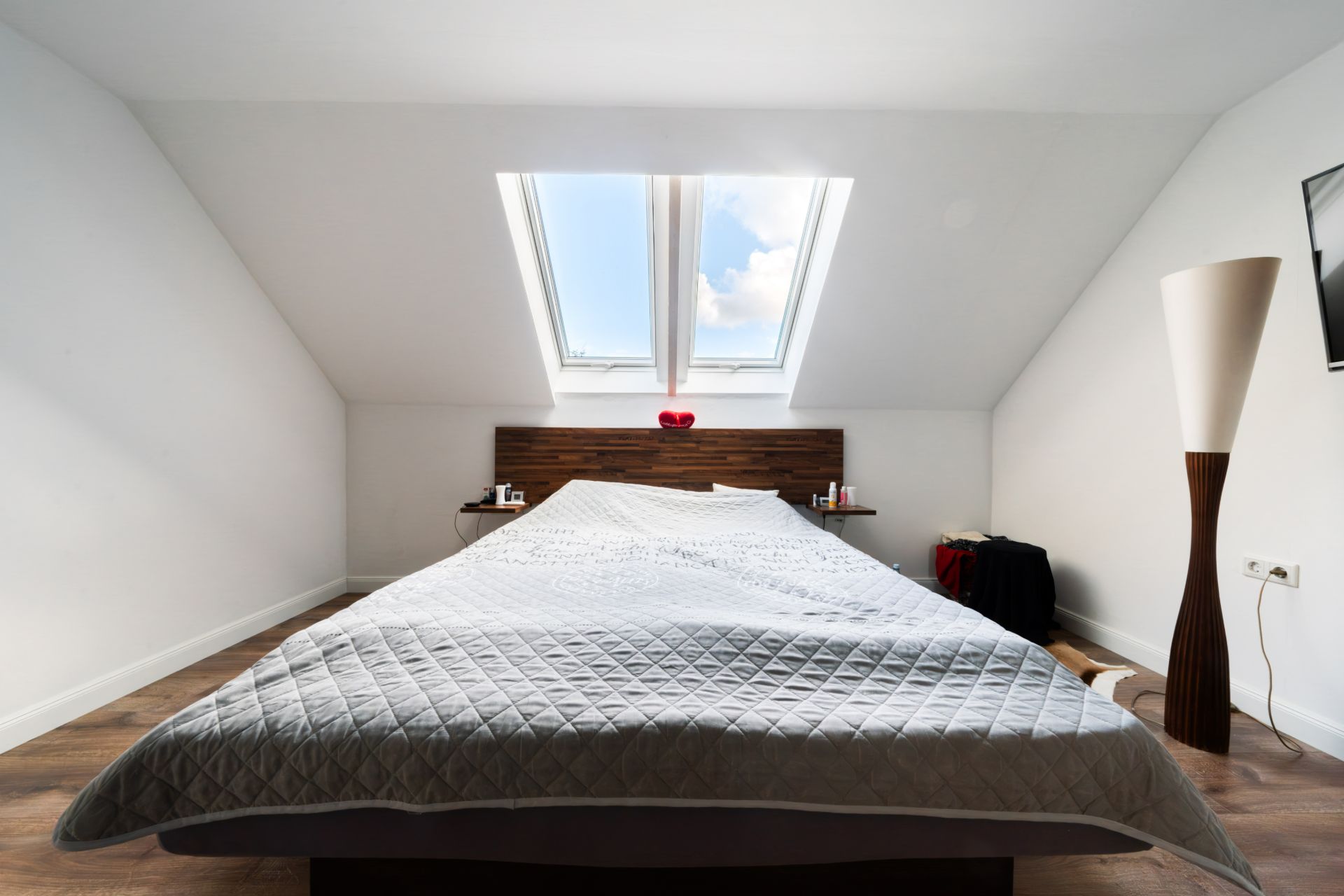 Modernes Schlafzimmer mit Bett, Dachfenster und Stehlampe in einem hellen Raum.