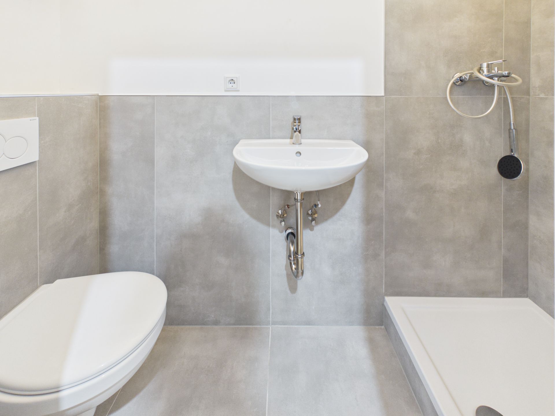 Modernes Bad mit Toilette, Waschbecken und Dusche, gefliest in hellgrau.
