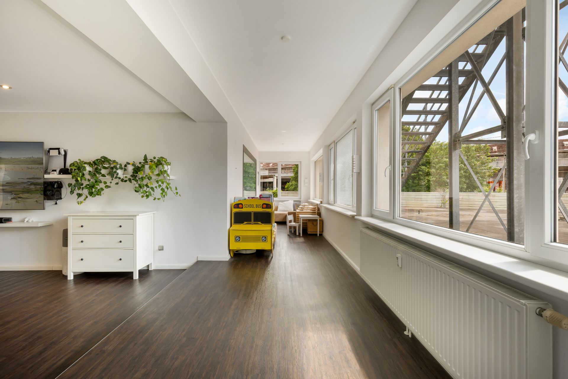 Heller Flur mit großen Fenstern, Holzfußboden und einem gelben Spielzeugbus.