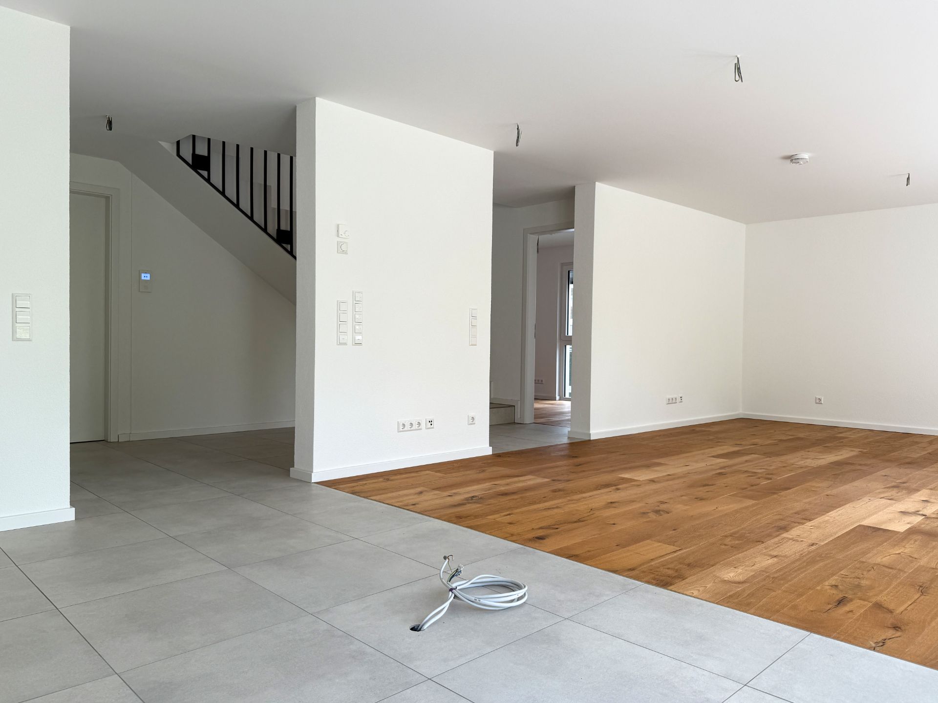 Leerer Wohnraum mit Fliesen- und Holzfußboden, Treppe und weißen Wänden.
