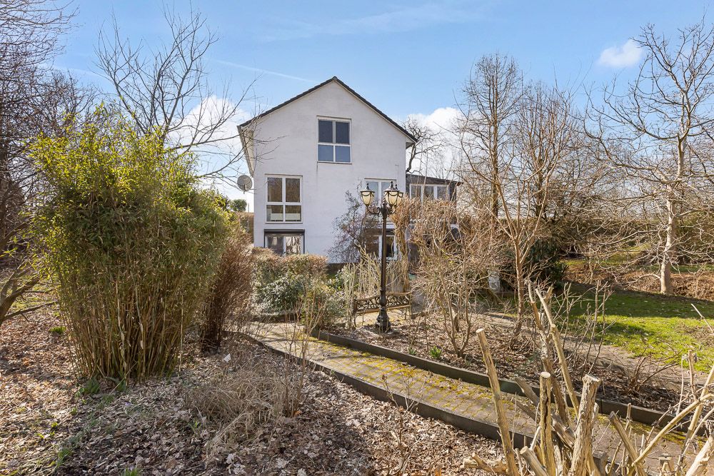 Weißes Wohnhaus mit Garten und Bäumen, Weg führt zum Eingang, Laterne im Vordergrund.