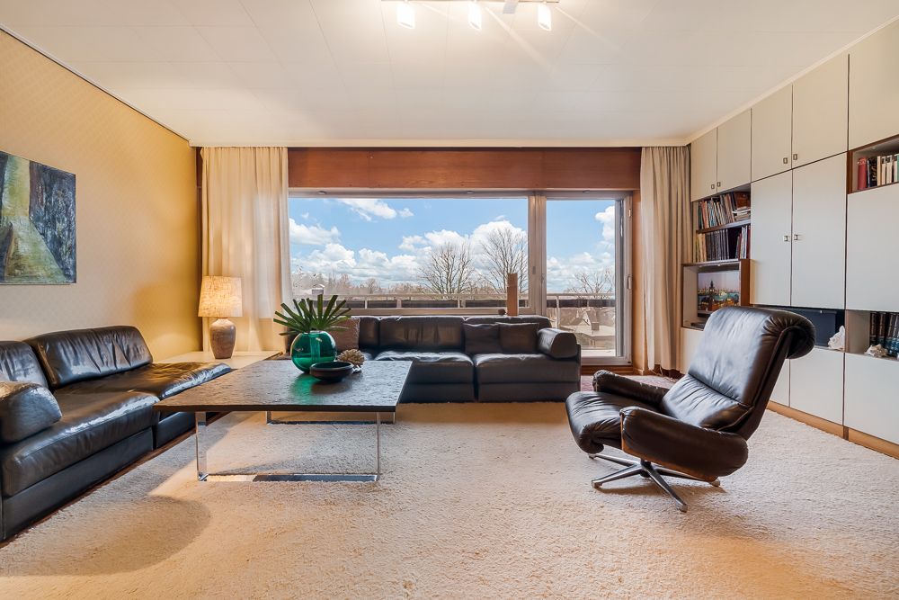 Wohnzimmer mit schwarzen Ledersofas, Sessel, großem Fenster und Einbauschränken.