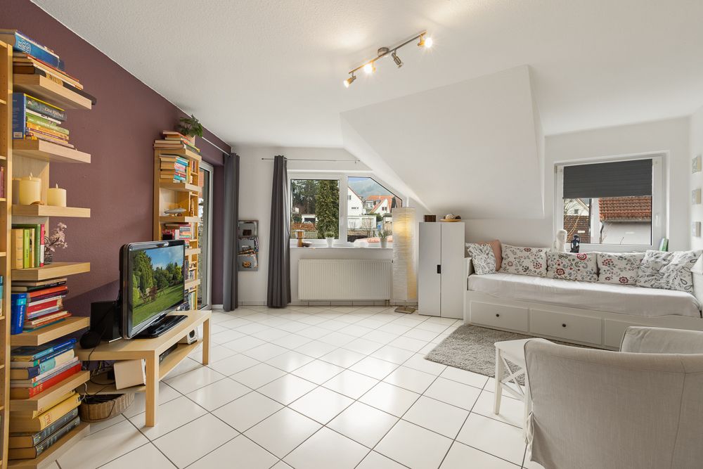 Helles Wohnzimmer mit Bücherregalen, Fernseher, Sofa und großen Fenstern mit Blick nach draußen.