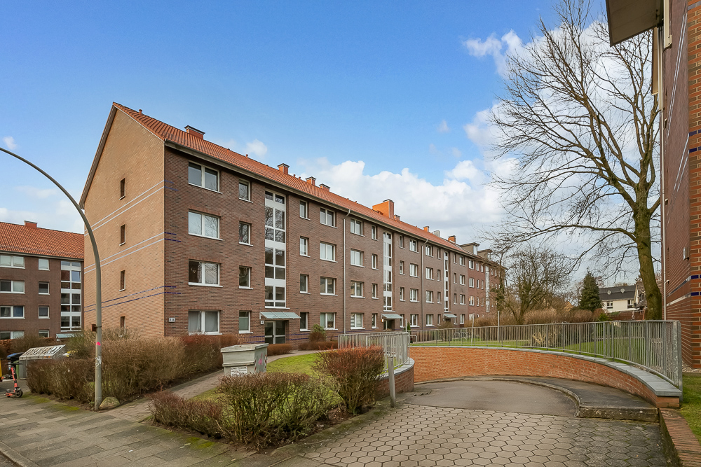 Viergeschossiges Mehrfamilienhaus aus Backstein mit Vorgarten und Gehweg bei Tageslicht.