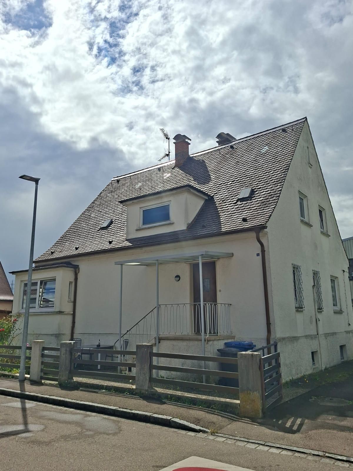 Einfamilienhaus mit Satteldach, Zaun und kleinem Vorgarten an einer Straße.