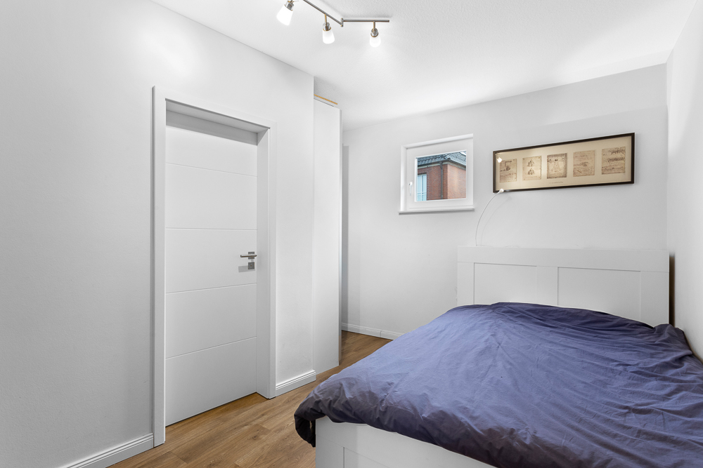 Helles Schlafzimmer mit einem Bett, Holzboden, Fenster und weißer Tür.