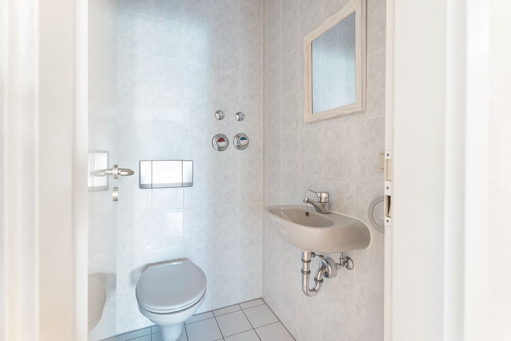 Kleines Badezimmer mit Toilette, Waschbecken und Spiegel an weiß gefliester Wand.