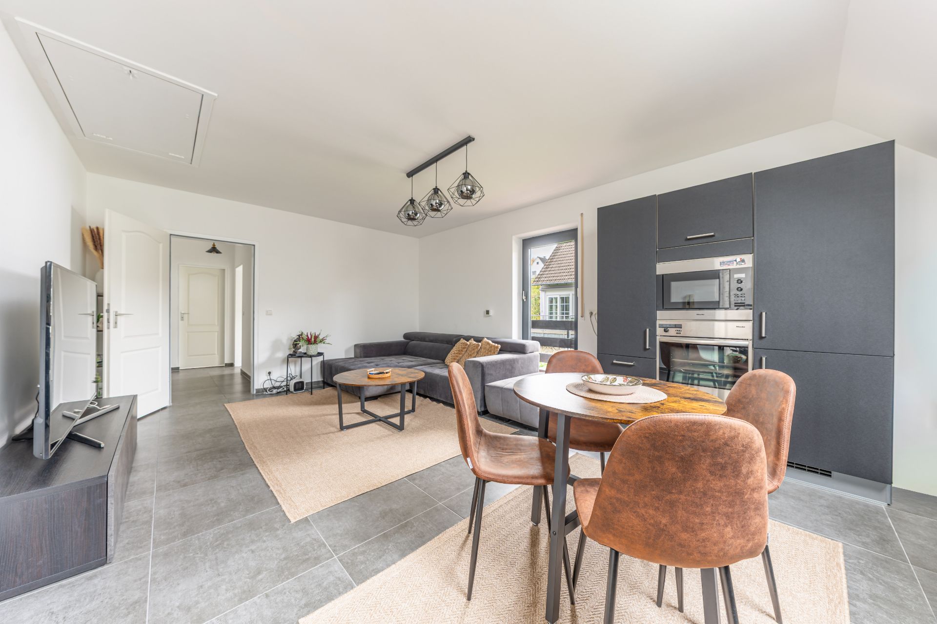 Modernes Wohnzimmer mit Essbereich, grauem Sofa, TV und offener Einbauküche.