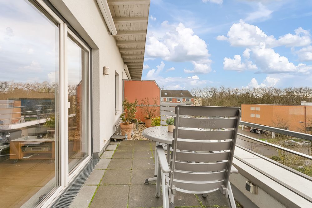 Balkon mit Tisch, Stuhl und Pflanzen, Blick auf Straße und Gebäude im Hintergrund.