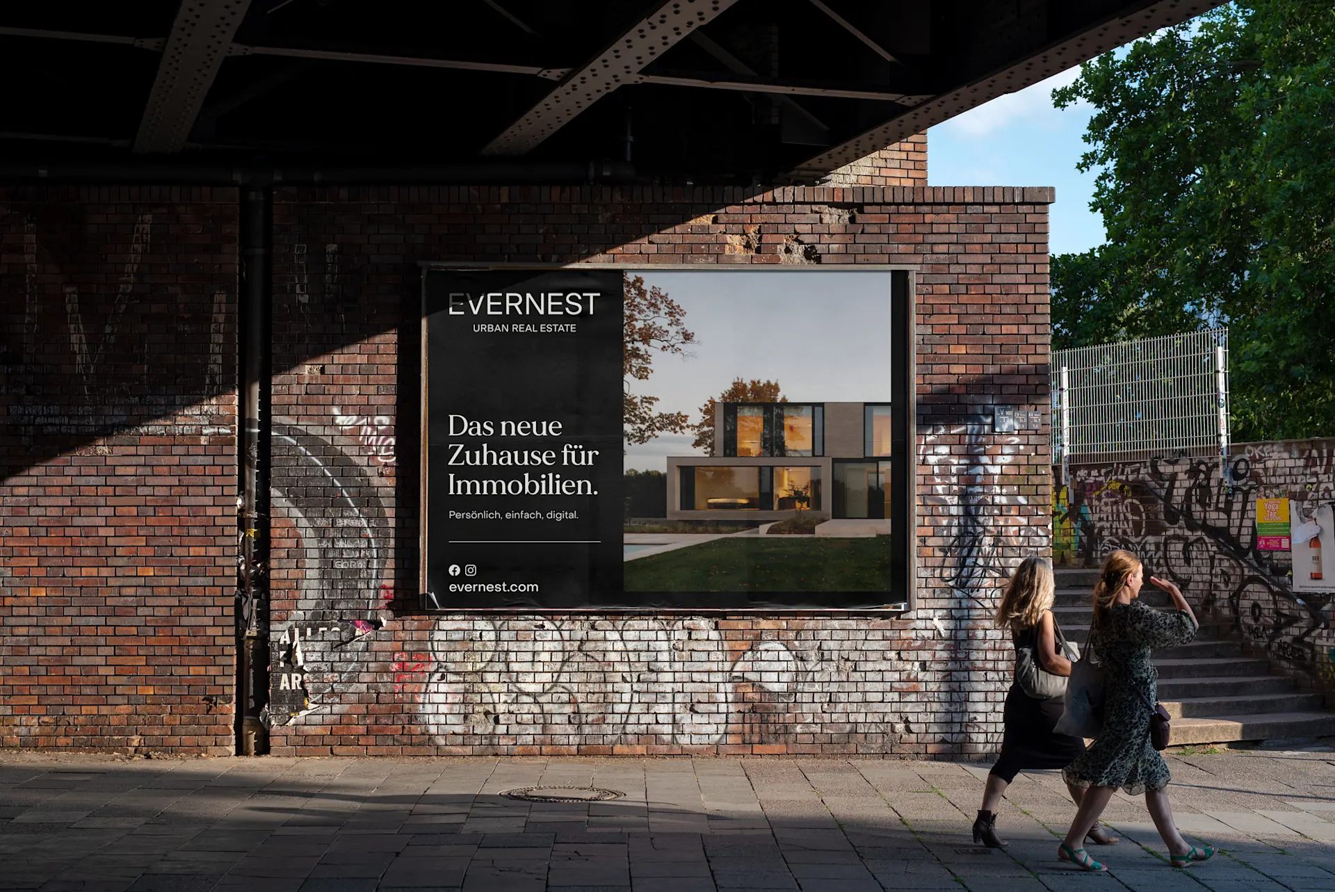 Werbeplakat mit modernem Wohnhaus an einer Backsteinmauer, zwei Frauen gehen davor vorbei.