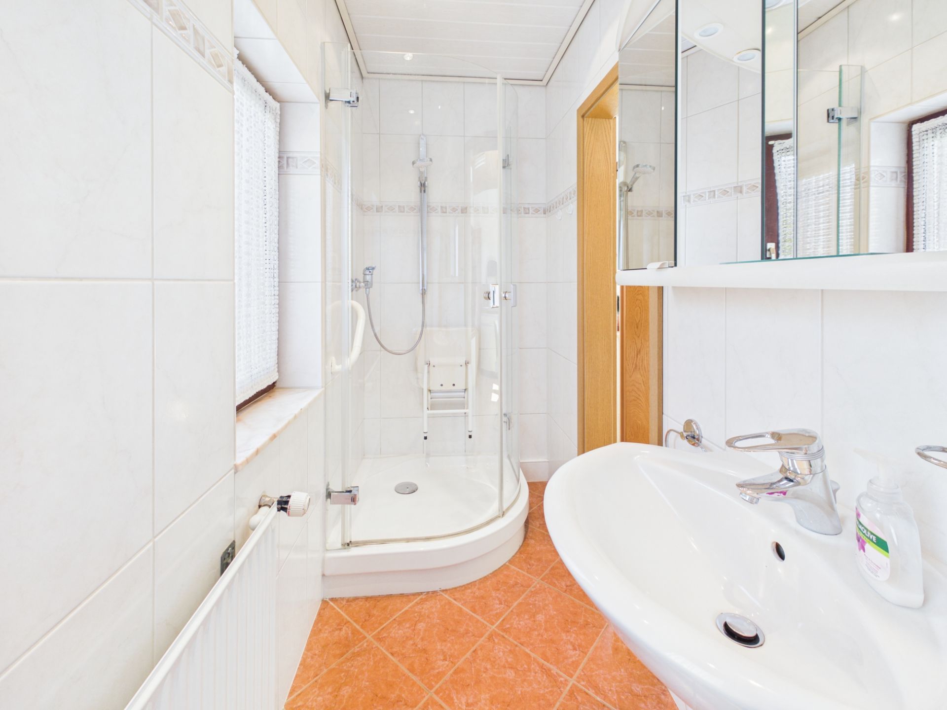 Helles Badezimmer mit Dusche, Waschbecken, Spiegel und Fenster.