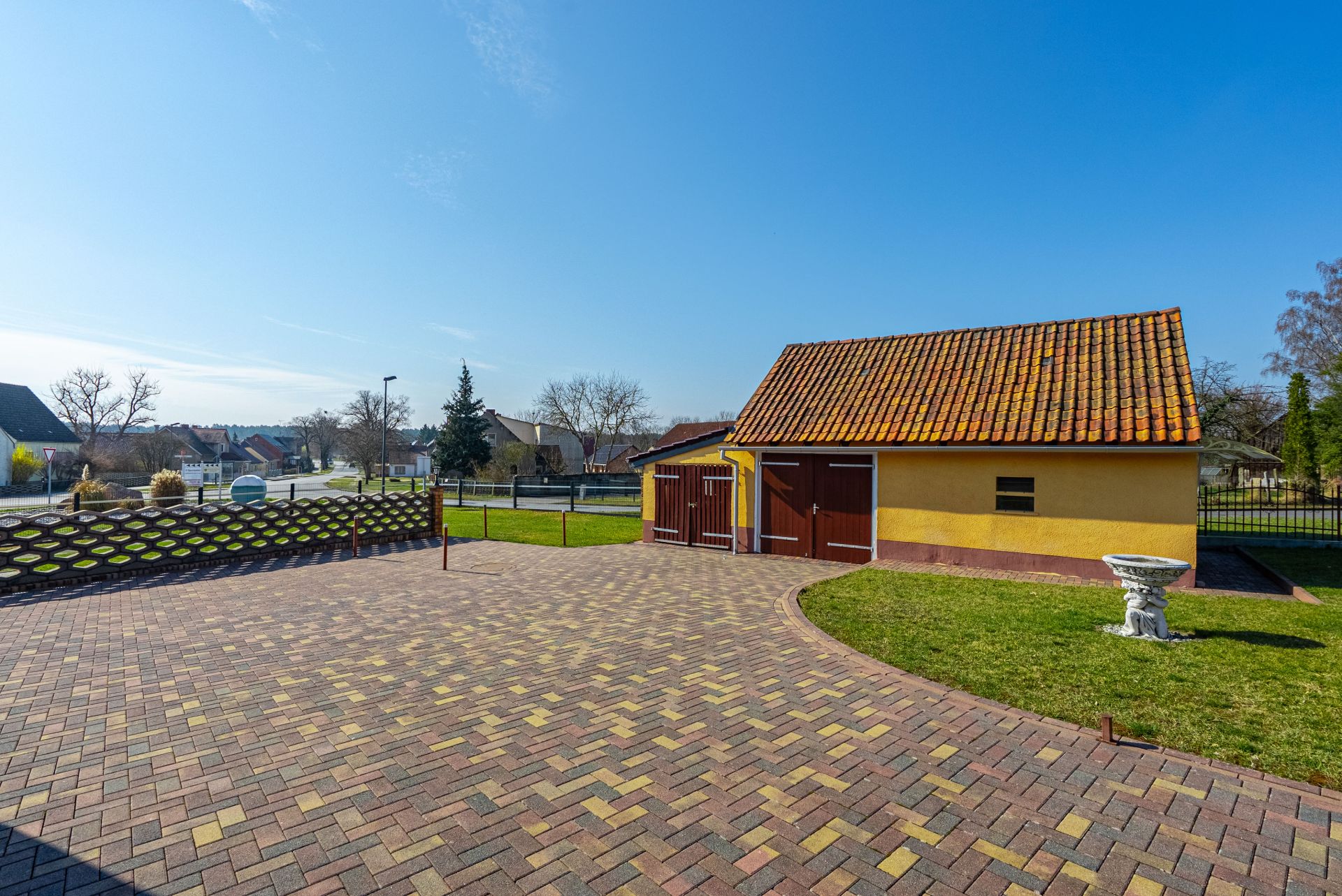Gepflasterter Hof mit Rasenfläche, gelbem Nebengebäude und Vogelbad im Garten.