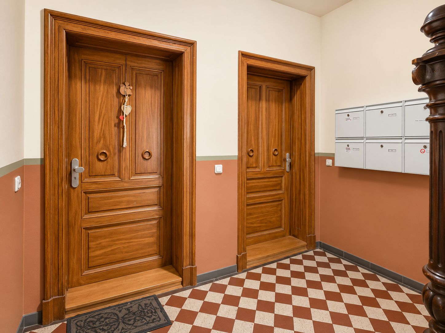 Flur mit zwei Holztüren, Briefkästen an der Wand und rot-weiß kariertem Boden.